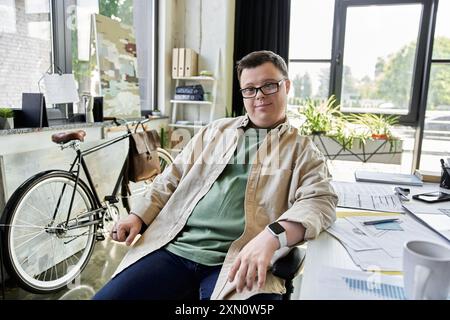 Ein junger Mann mit Down-Syndrom sitzt an einem Schreibtisch in einem modernen Büro und schaut in die Kamera. Stockfoto