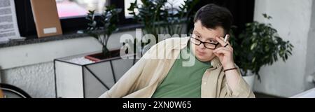 Ein junger Mann mit Down-Syndrom sitzt in einem Raum, verloren in Gedanken. Stockfoto