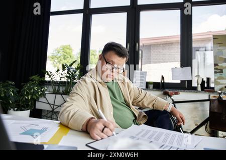 Ein junger Mann mit Down-Syndrom sitzt an einem Schreibtisch und konzentriert sich darauf, Papiere auszufüllen. Stockfoto