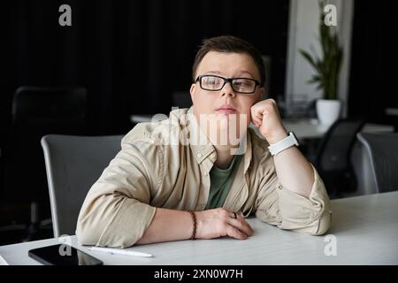 Ein junger Mann mit Down-Syndrom sitzt an einem Schreibtisch, legt sein Kinn auf seine Hand und denkt darüber nach. Stockfoto