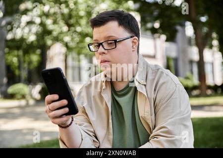 Ein Mann mit Down-Syndrom sitzt in einem Park und konzentriert sich auf sein Smartphone. Stockfoto