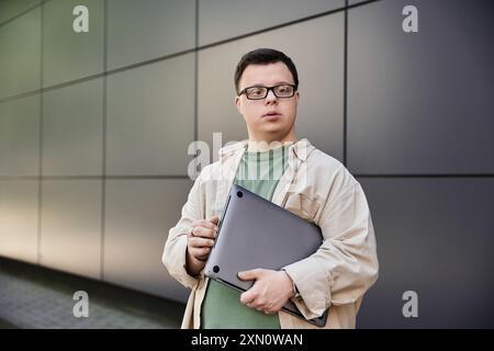 Ein junger Mann mit Down-Syndrom steht draußen und hält einen Laptop. Stockfoto