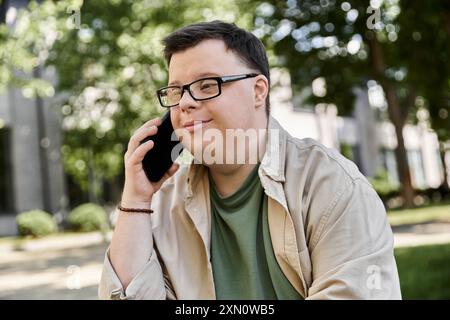 Ein Mann mit Down-Syndrom sitzt draußen und redet mit seinem Telefon. Stockfoto