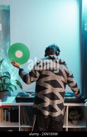 Ein Mann hält Schallplatten in der Nähe des Plattenspielers in einem gemütlichen Zimmer Stockfoto