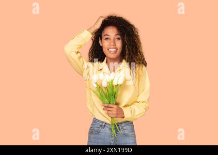 Lächelnde Frau, die Tulpen vor Peach-Hintergrund hält Stockfoto