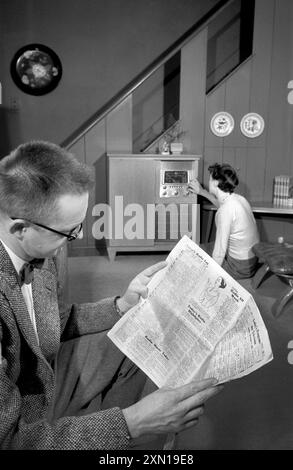 Mann, der Zeitung liest, während die Frau im Wohnzimmer das Wahlrad dreht, Warren K. Leffler, U.S. News & World Report Magazine Photographie Collection, 1957 Stockfoto