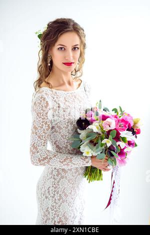 Fröhliche Mädchen Braut in einem weißen Strickkleid posiert mit Ein Blumenstrauß im Atelier auf einem weißen Hintergrund Stockfoto