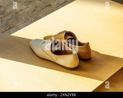 Ein Paar luxuriöse Damenschuhe, die auf Holzregalen ausgestellt sind und kontrastierende Schatten darauf fallen, schaffen eine elegante und raffinierte Präsentation in einem High-End-Einzelhandelsumfeld Stockfoto