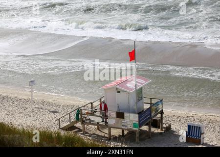 Rettungsturm mit roter Flagge am Strand von Westerland, Sylt DEU, Deutschland, Sylt, Westerland: Das Bild zeigt einen Rettungsturm am Strand von Westerland auf Sylt. Eine rote Flagge weht im Wind, was auf ein Badeverbot und Lebensgefahr hinweist. Der Rettungsturm steht auf Stelzen und im Hintergrund sind die stürmische Nordsee und der breite Sandstrand zu sehen. Westerland Sylt Schleswig Holstein Deutschland *** Rettungsturm mit roter Flagge am Strand von Westerland, Sylt DEU, Deutschland, Sylt, Westerland das Bild zeigt einen Rettungsturm am Strand von Westerland auf Sylt winkt Eine rote Flagge in t Stockfoto