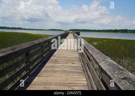 Ein langer Holzsteg, der sich über Sumpfgebiete erstreckt und zu einem fernen Horizont unter einem teilweise bewölkten Himmel führt Stockfoto