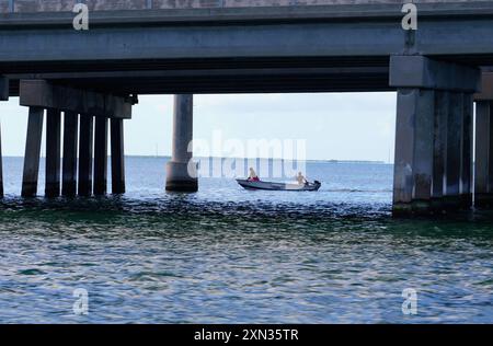 Zwei Personen fischen unter einer Brücke in einem kleinen Boot und genießen einen friedlichen Tag auf dem Wasser. Stockfoto