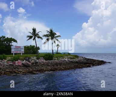 Eine ruhige Küstenlandschaft mit Palmen am Ufer und einem Schild mit der Aufschrift „U.S. Government Property, No Trespassing“ Stockfoto