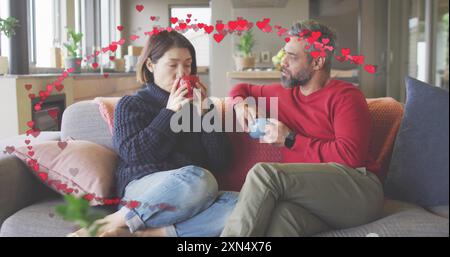 Das Bild von Herzen über verschiedene Paare, die auf dem Sofa sitzen und zu Hause Kaffee trinken Stockfoto