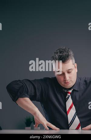 Ein reifer Geschäftsmann im Alter von 40 Jahren lehnt sich nachdenklich auf einen eleganten Schreibtisch in einem modernen Büro und strahlt Professionalität und Konzentration aus Stockfoto