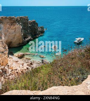 Atemberaubende Küstenlandschaft mit einem Boot, das in klarem blauem Wasser in der Nähe von felsigen Klippen schwimmt, bietet natürliche Schönheit und Ruhe. Stockfoto