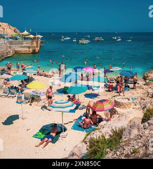 Ein geschäftiger Strand an einem sonnigen Tag mit Leuten, die sich unter bunten Sonnenschirmen entspannen, schwimmen und das Sommermeer genießen. Stockfoto