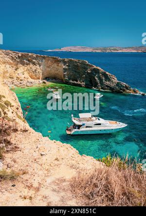 Ein malerischer Blick auf Luxusyachten, die an einem sonnigen Tag im kristallklaren blauen Wasser in der Nähe einer felsigen Küste ankern. Stockfoto