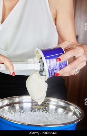Frau, die Tiramisu-Dessert in Metallschüssel mit Schüssel an der Seite in der Küche zubereitete. Schritt-für-Schritt-Rezept. Stockfoto