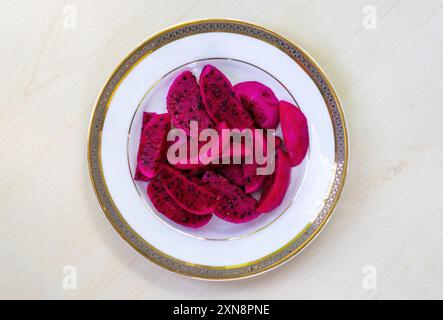 Drachenfrucht geschnittene Stücke auf einer weißen Platte auf hölzernem Hintergrund. Es ist auch bekannt als pitaya oder Pitahaya. Draufsicht. Stockfoto