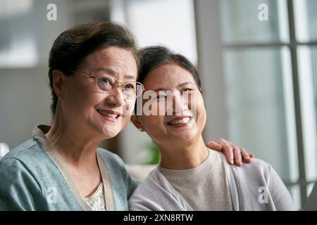 Porträt von zwei älteren asiatischen Frauen, die zu Hause glücklich und lächelnd auf der Couch sitzen Stockfoto