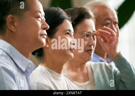 Seitenansicht einer Gruppe älterer asiatischer Leute, zwei Paare, die zu Hause auf der Couch sitzen und fernsehen Stockfoto