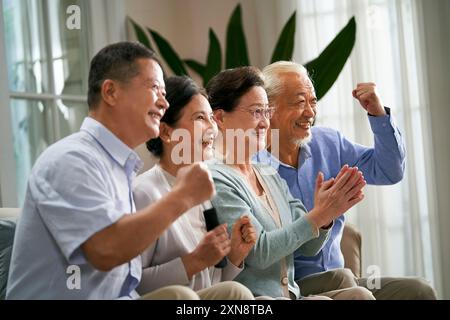 Gruppe glücklicher älterer asiatischer Leute, zwei Paare, die zu Hause auf der Couch sitzen und gemeinsam Sportspiele im fernsehen ansehen Stockfoto