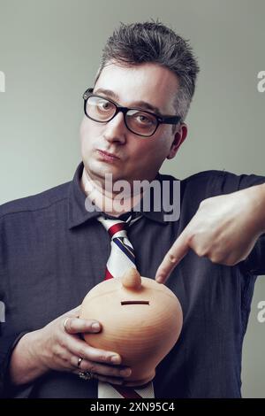 Ein besorgter Buchhalter hält eine leere Sparkasse, die Finanzkämpfe und Investitionsherausforderungen symbolisiert Stockfoto