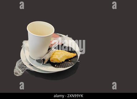 Leere weiße Kaffeetasse und übriggebliebener Snack auf weißem Teller auf schwarzem Hintergrund. Szene nach dem Essen. Stockfoto