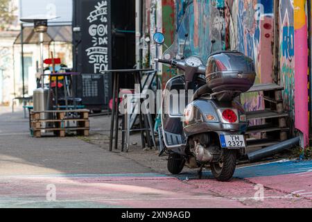 Riga, Lettland - 30. September 2020: Ein geparkter Roller ruht neben farbenfroher Straßenkunst in einem belebten Außenbereich. Stockfoto