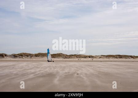 Eine Landyacht, die über den flachen Sand des Sankt-Peter-Ording-Strandes fährt. Landsegeln ist ein beliebter Sport in diesem Badeort an der deutschen Nordseeküste. Ein konstanter Wind treibt Sand- und Staubwolken über die Wattgebiete. Stockfoto