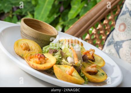 Ein Teller mit knusprigen goldenen Pfannkuchen, garniert mit prallen Garnelen und serviert mit einem Salat wird auf einem weißen Tisch präsentiert Stockfoto