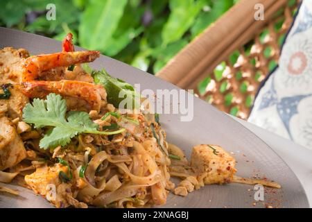 Ein Teller Pad thai mit gebratenen Reisnudeln, Tofu, Huhn und Garnelen, garniert mit gemahlenen Erdnüssen, Koriander und einem Limettenkeil Stockfoto