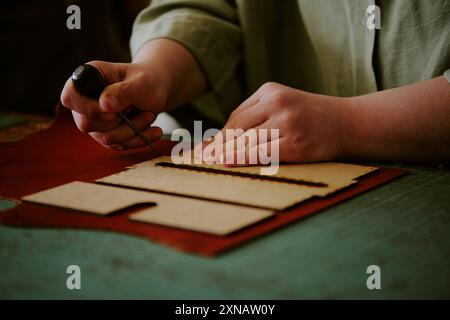 Mittlere Nahaufnahme von nicht erkennbaren weiblichen Händen, die Lederstück unter Verwendung einer Axt stechen Stockfoto