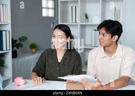 Junge Paare diskutieren mit Piggy Bank über Finanzpläne und Sparen in modernem Home Office Setting Stockfoto