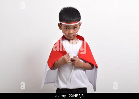 Süßer kleiner asiatischer Junge, der Haarband und Gewand mit indonesischer Flagge trägt. Konzept des Unabhängigkeitstages Indonesiens am 17. August Stockfoto