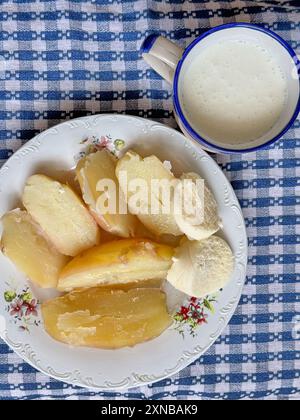 Traditionelles Frühstück mit gekochten Kartoffeln und Käse, serviert mit einer Tasse Sauermilch auf einer dekorativen Tischdecke Stockfoto