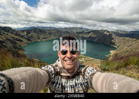 Ein multirassischer hispanischer junger Mann macht ein Selfie mit einer Kamera vor der malerischen Quilotoa-Lagune in Ecuador. Das Bild erfasst den lebendigen tur Stockfoto