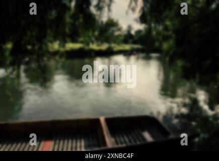 Ein verschwommenes Bild eines hölzernen Ruderbootes, das in einem Fluss sitzt, mit einem üppigen, grünen Wald im Hintergrund. Die Oberfläche des Flusses ist reflektierend, und der Wald Stockfoto