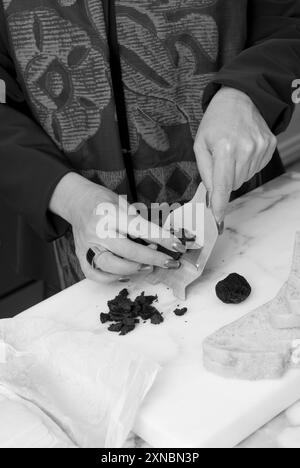 Nahaufnahme von weiblichen kaukasischen Händen, die schwarze Diamanttrüffel schneiden, um ein Gourmet-Sandwich mit Sauerteigbrot zuzubereiten. USA Stockfoto