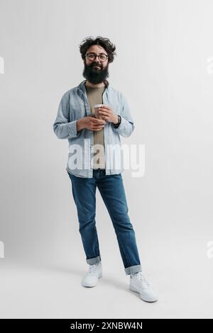 Glücklicher bärtiger Mann in lässigen Kleidern, der eine Kaffeetasse hält Stockfoto