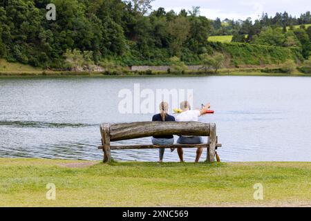 Ein paar Touristen sitzen auf einer Bank und genießen die magische Landschaft des Furnas-Sees (Lagoa das Furnas) Sao Miguel, Azoren Stockfoto