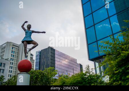 In der Stadt steht eine anmutige Ballerina-Skulptur, die einem hochaufragenden Wolkenkratzer gegenübersteht und Kunst mit urbaner Architektur für ein eindrucksvolles Bild verbindet. Stockfoto