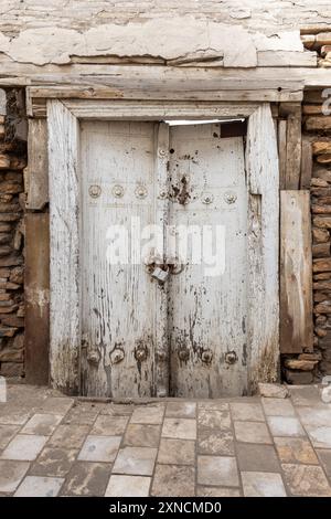 Alte weiße Holztür in alte Steinmauer, Nahansicht von vorne. Vertikales Foto in der Altstadt von Buchara, Usbekistan Stockfoto