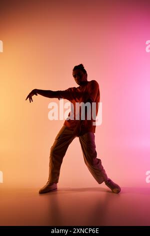 Ein männlicher afroamerikanischer Tänzer posiert vor einem lebendigen Hintergrund mit Farbverlauf und zeigt seine dynamischen Bewegungen. Stockfoto