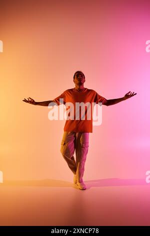 Ein männlicher afroamerikanischer Tänzer posiert mit ausgestreckten Armen unter farbenfroher Beleuchtung. Stockfoto