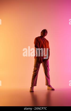 Ein männlicher afroamerikanischer Tänzer posiert vor einem lebendigen Hintergrund mit Farbverlauf, beleuchtet durch buntes Licht. Stockfoto