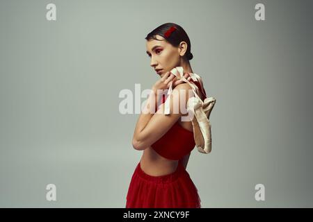 Eine junge Frau mit kurzen Haaren, die ein rotes Oberteil und einen Minirock trägt, posiert mit Ballettschuhen in der Hand. Stockfoto