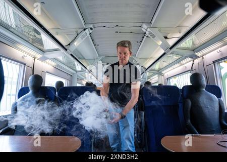 Minden, Deutschland. 31. Juli 2024. Daniel Schmeling, Deutsches Zentrum für Luft- und Raumfahrt (DLR), sprüht in einem Testwagen der Deutschen Bahn mit einer Rauchmaschine Rauch in den Zugraum, um die Luftturbulenzen für Fahrgäste zu testen. Das Deutsche Zentrum für Luft- und Raumfahrt (DLR) in Göttingen erforscht Klimaanlagen für Züge in einem Prüfwagen der Deutschen Bahn. Quelle: Guido Kirchner/dpa/Alamy Live News Stockfoto