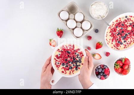 Kochen Herstellung von gebackenem Joghurt gesundes Dessert. Frau Hand kochen Ofen gebacken griechischer Joghurt Dessert mit frischen gefrorenen Beeren, auf weißem Küchentisch, mit Stockfoto