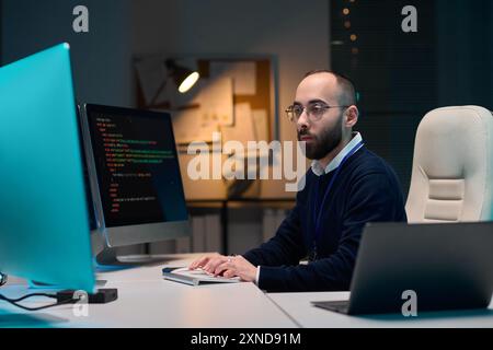 Porträt eines bärtigen Mannes mittleren Alters mit Brille und Computer im Blaulicht-Kopierraum Stockfoto